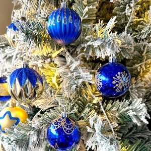 Blue and gold Christmas ball ornaments with snowflake patterns on a frosted tree with lights