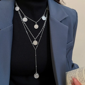 Detail of silver layered coin necklace with angel relief pendant on a black turtleneck