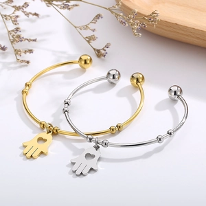 Golden and silver Hamsa hand open bangles with heart charms on a wooden tray
