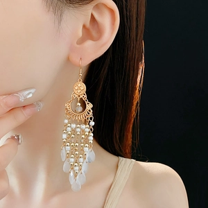 Detail view of golden floral earrings with layered white bead tassels on a model