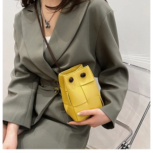 Detail of yellow woven bucket bag with knotted strap on a green blazer outfit