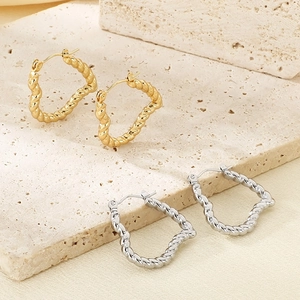 Detailed view of gold and silver twisted heart earrings on a natural textured stone base