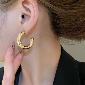 Close-up of a model wearing a thick golden C-shaped hoop earring with a polished finish
