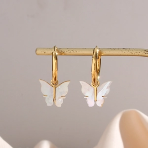 Gold hoop earrings featuring elegant white butterfly shell pendants on a metal stand