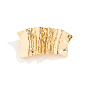 Close-up of golden liquid metal hair clip with irregular wave texture and mirror finish