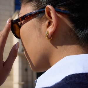 Close-up of a model wearing twisted gold stainless steel C-shaped earrings with zircon