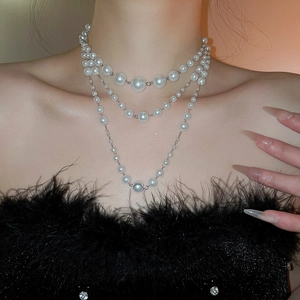 Close-up of elegant triple-layered pearl necklace on model with black feather outfit