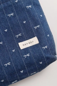 Close-up of denim cosmetic bag featuring white embroidered bows and heart patterns