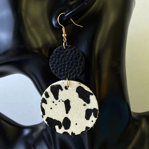 Boucles d'oreilles en cuir motif vache avec clous ronds noirs sur un mannequin