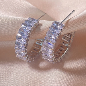 Vue macro de créoles argentées en C avec zircons rectangulaires sur soie rose pastel