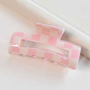 Close-up of pink and beige checkered acetate hair claw clip on soft beige fabric