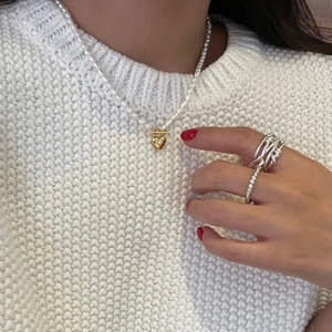 Close-up of pearl necklace with gold heart pendant and silver textured ring on model