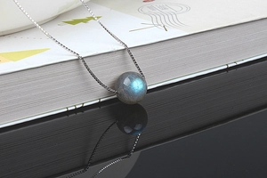 Macro shot of a glowing blue labradorite pendant on a silver box chain with reflection
