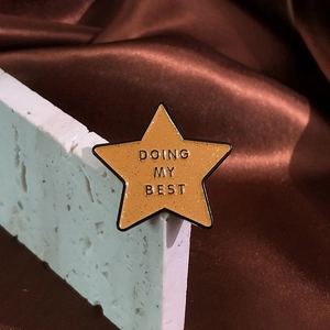 Pentagram star enamel pin with Doing My Best text on white stone and brown satin background