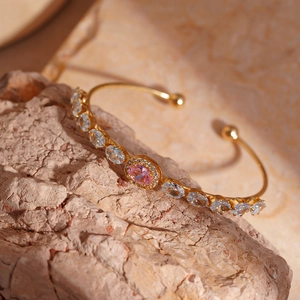 Detailed macro of gold open bangle with pink and blue oval gemstones on a stone surface