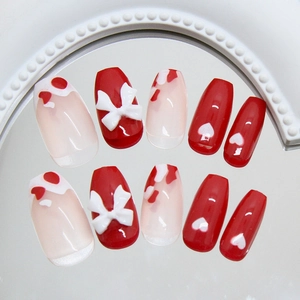 Red and white press-on nails with bow accents, cow print, and heart designs