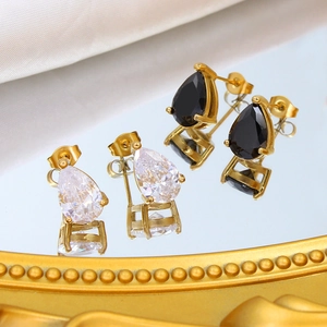 Golden teardrop earrings with black and white zircon stones on a luxury mirror surface