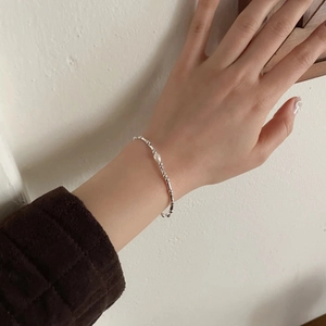 Detailed view of a silver-toned thin chain bracelet featuring a single white pearl on a wrist