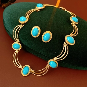 Detail of vintage gold jewelry set with oval turquoise stones on a green velvet cushion