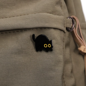 Detalle de un mini pin de gato negro esmaltado con ojos amarillos en bolso de tela
