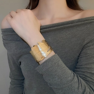 Detail of a golden leaf-shaped wide cuff bracelet on a model's wrist with metallic shine