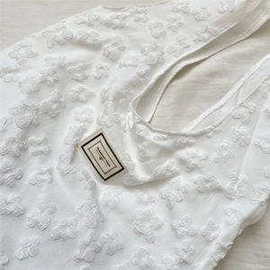 Macro detail of white jacquard tote bag featuring 3D floral textures and fabric label
