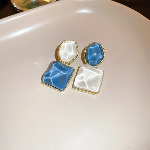 Macro shot of asymmetric resin earrings with blue and white water ripple texture and gold edges