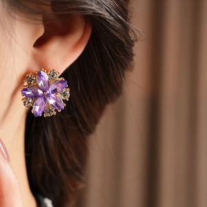 Primo piano di orecchini floreali vintage con petali viola e cristalli lucidi su modella