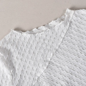 Détail de la robe en tricot blanc montrant la texture plissée et la finition du décolleté