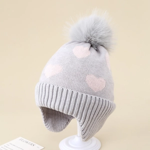 Close-up of grey knit hat featuring pink heart pattern and a fluffy faux fur pom-pom