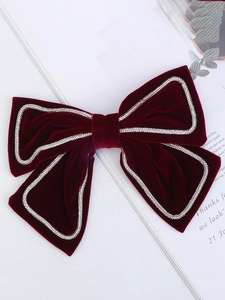 Detail of burgundy velvet hair bow with sparkling silver rhinestone trim on white background