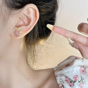 Elegant pink rose stud earrings with gold trim and crystal leaves on model's ear