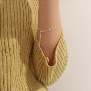 Detail of a minimalist S925 sterling silver snake chain bracelet on a yellow knit sweater