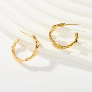 Chic golden C-shaped hoop earrings with irregular wavy texture on stone display