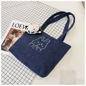 Detailed view of navy corduroy tote bag with white rabbit embroidery and cow plush charm