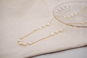 Close-up of a long golden necklace with baroque pearls on a textured beige fabric