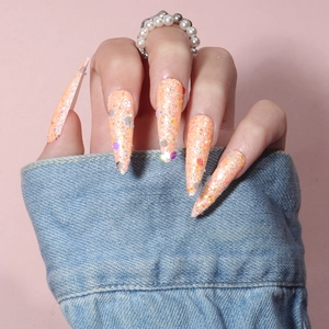 Macro view of long stiletto orange glitter press-on nails with colorful sequins