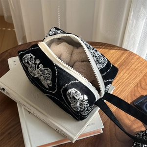 Detailed white butterfly embroidery on a black canvas handheld bag with white zippers