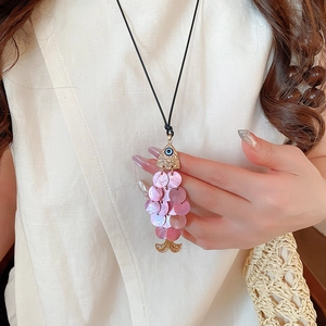 Close-up of golden fish pendant with pink shell scales and blue eye gem necklace