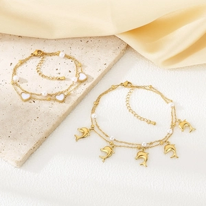 Detailed view of double-layer gold anklet with heart and dolphin charms on silk