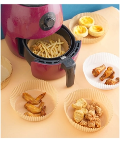 Close-up of brown and white round air fryer parchment liners with fries and chicken wings