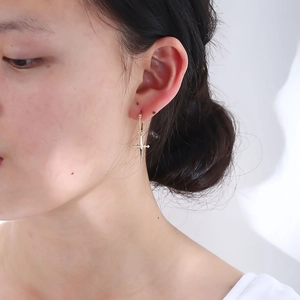 Macro detail of a 925 silver gold-plated cross drop earring worn on a female model