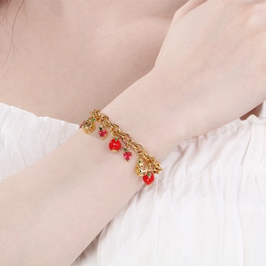 Close-up of a gold fruit charm bracelet with red strawberry and heart pendants on a wrist