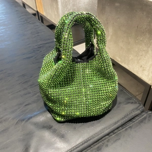 Detailed view of shimmering emerald green rhinestone bucket bag on a luxury leather seat