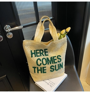 Close-up of woven straw tote with Here Comes The Sun green embroidery and hollow mesh detail