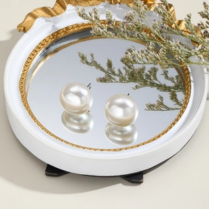 Detail of round cream pearl earrings on a vintage gold-edged mirror tray with soft lighting