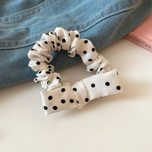 Close-up of cream satin scrunchie with black polka dots and a matching bow decoration