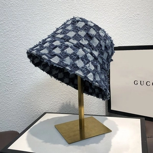 Detailed view of checkered bucket hat with frayed edges on a gold metal stand