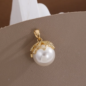 Macro shot of white round pearl pendant with textured gold crown cap on leather background