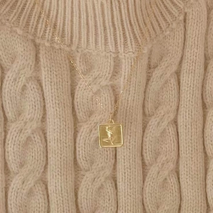 Vintage gold square floral pendant necklace on warm beige knit sweater background